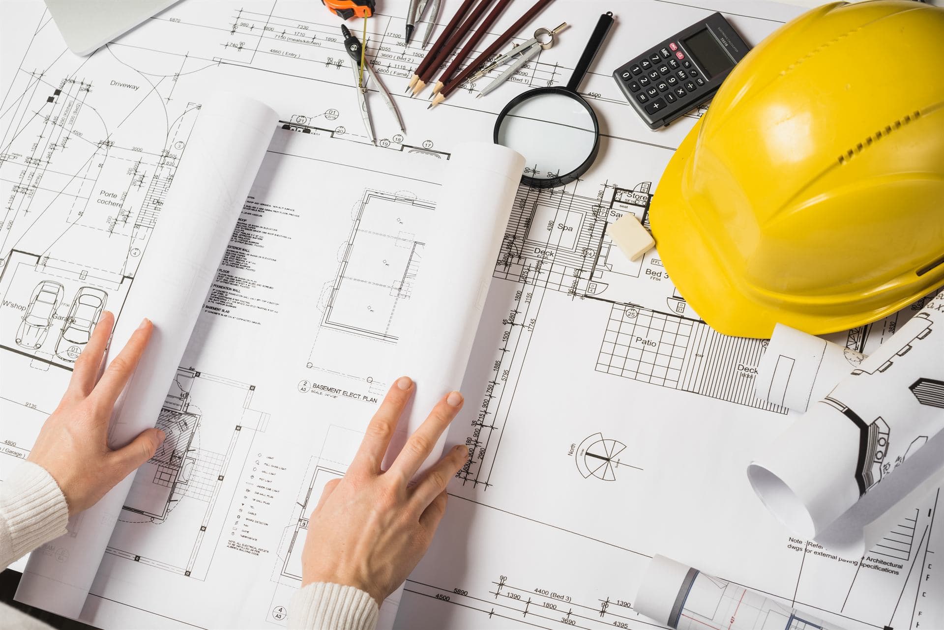 Planos de obra sobre una mesa, con casco de seguridad, calculadora y herramientas de medición